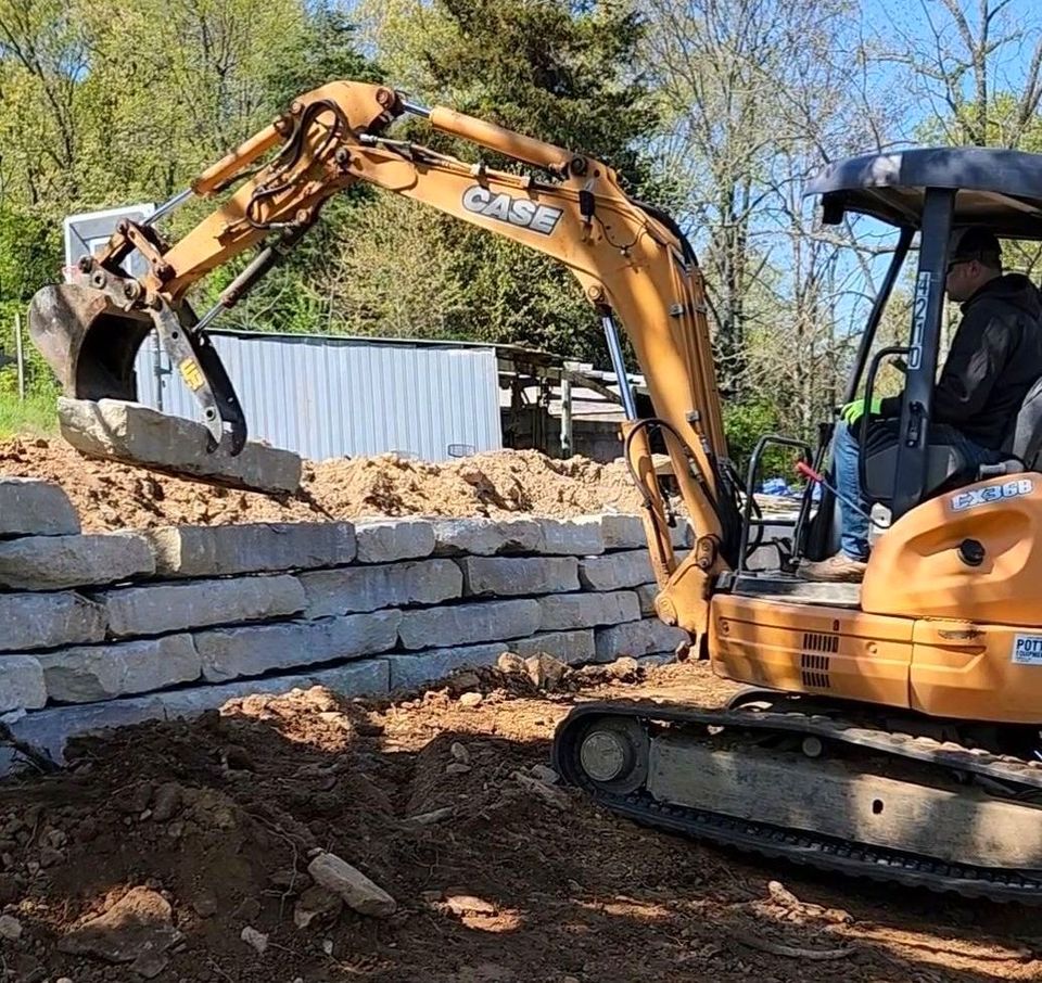 Yellow excavator placing limestone on top of a retaining wall. Rough Cuts Construction uses an excavator like this.