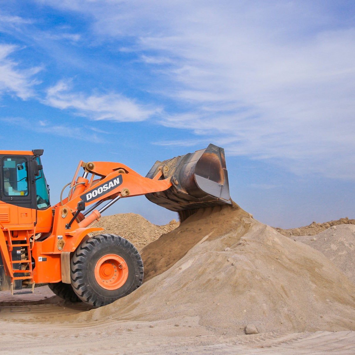 Large backhoe dumping sand on a large pile of sand.