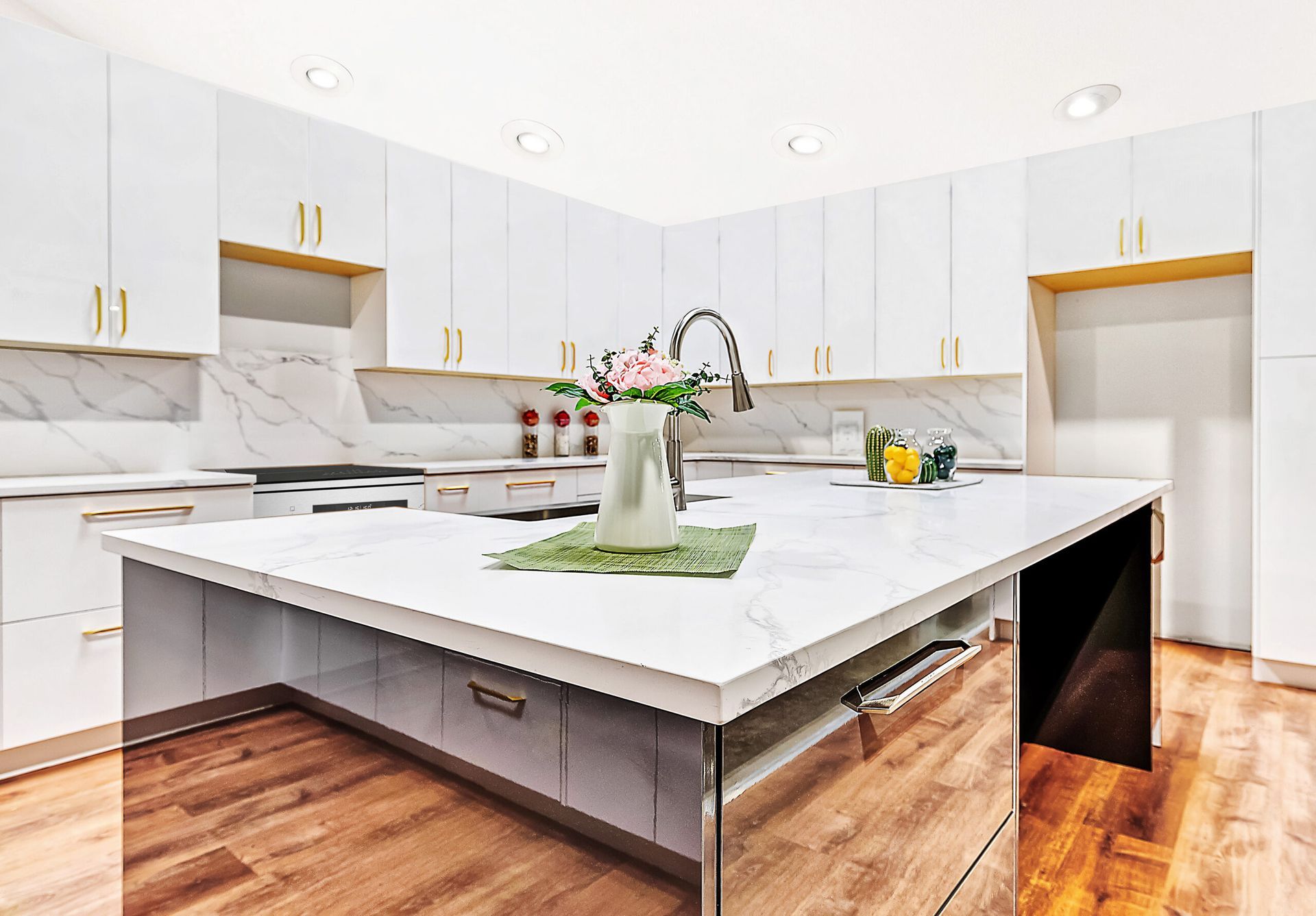 Modern white kitchen with a large island, marble countertops, and gold accents.