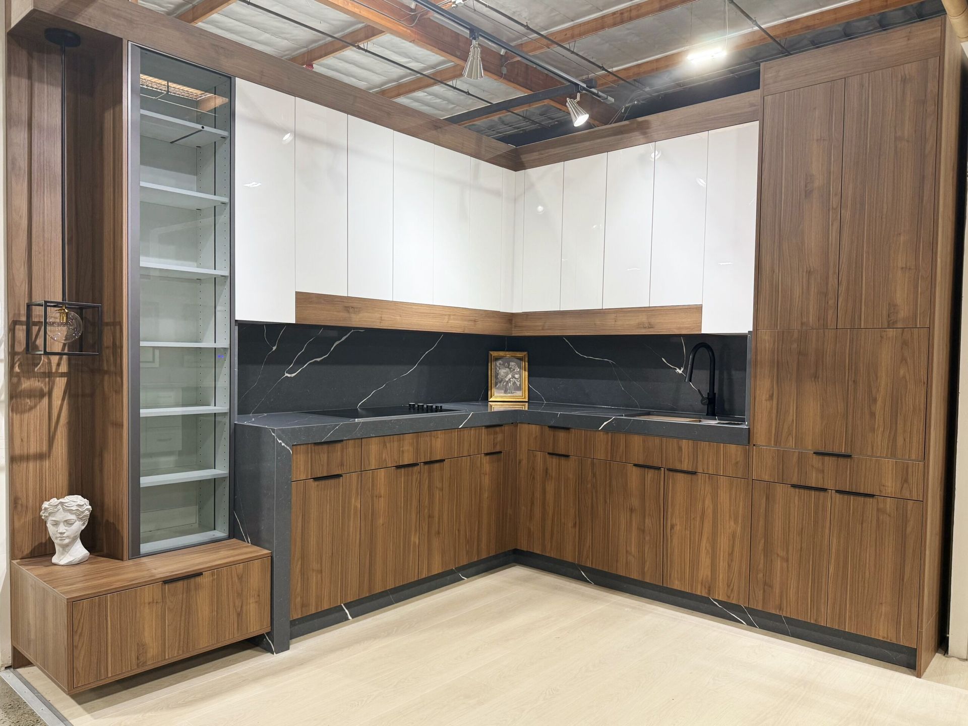 Modern kitchen with brown and white cabinets, black countertop, and glass-front display cabinet.