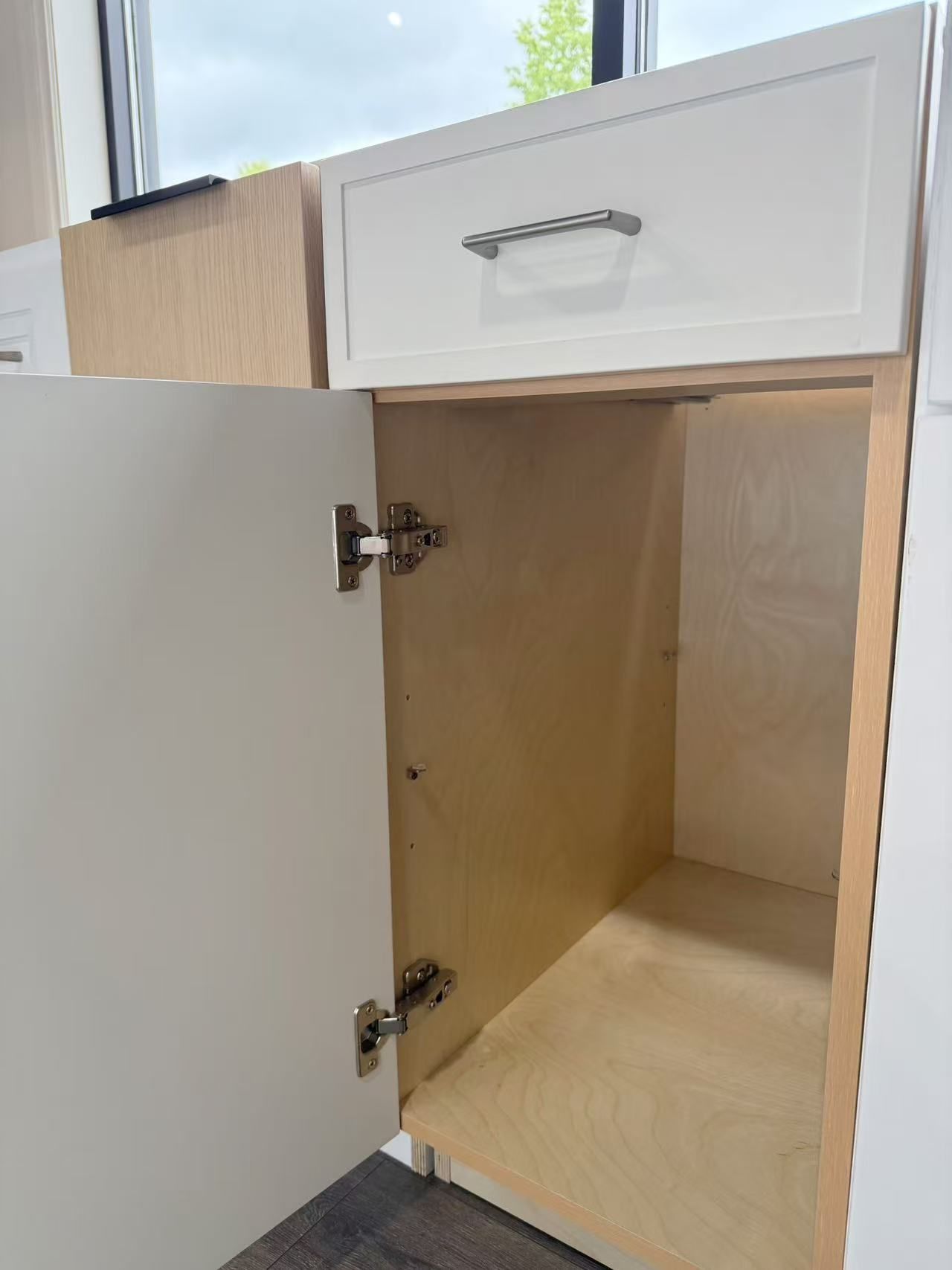 Open white kitchen cabinet with drawer above, revealing light-colored interior.