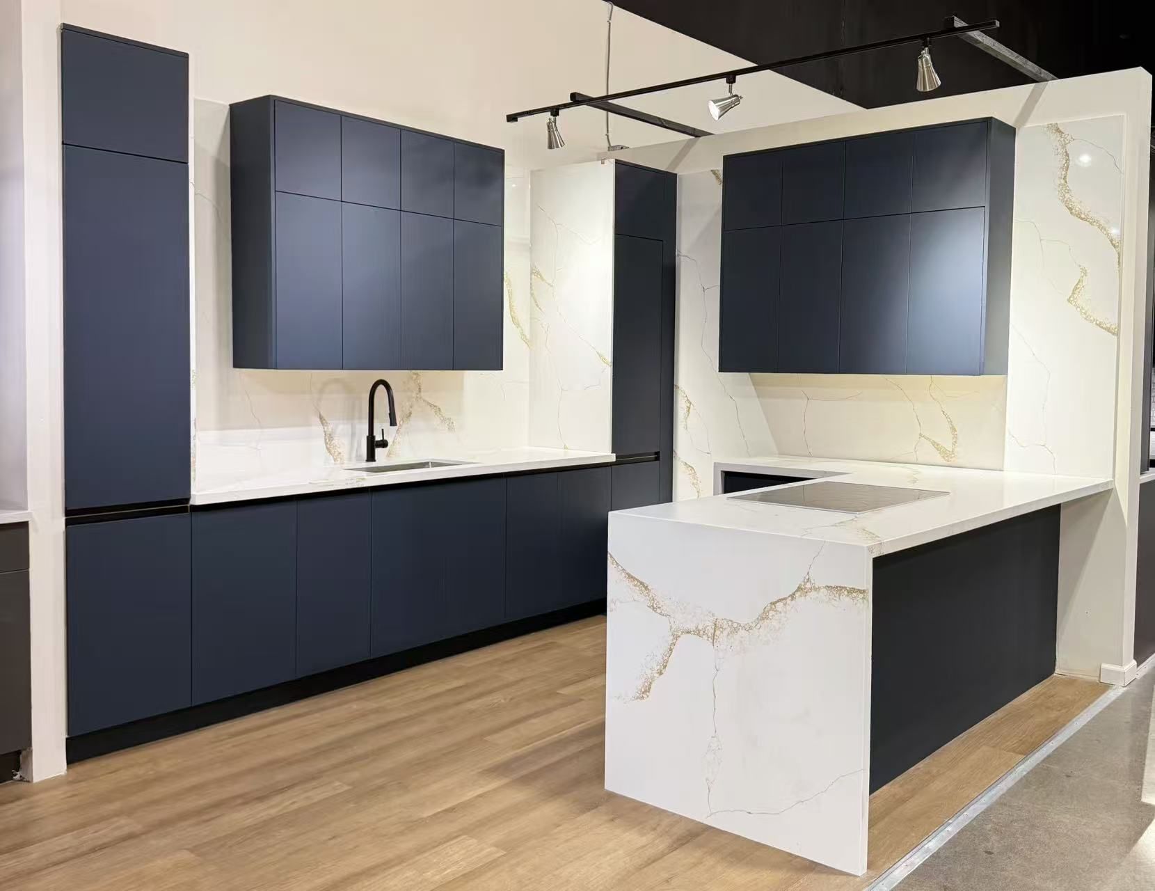 Modern kitchen with navy blue cabinets, white countertops with gold veining, and an island.