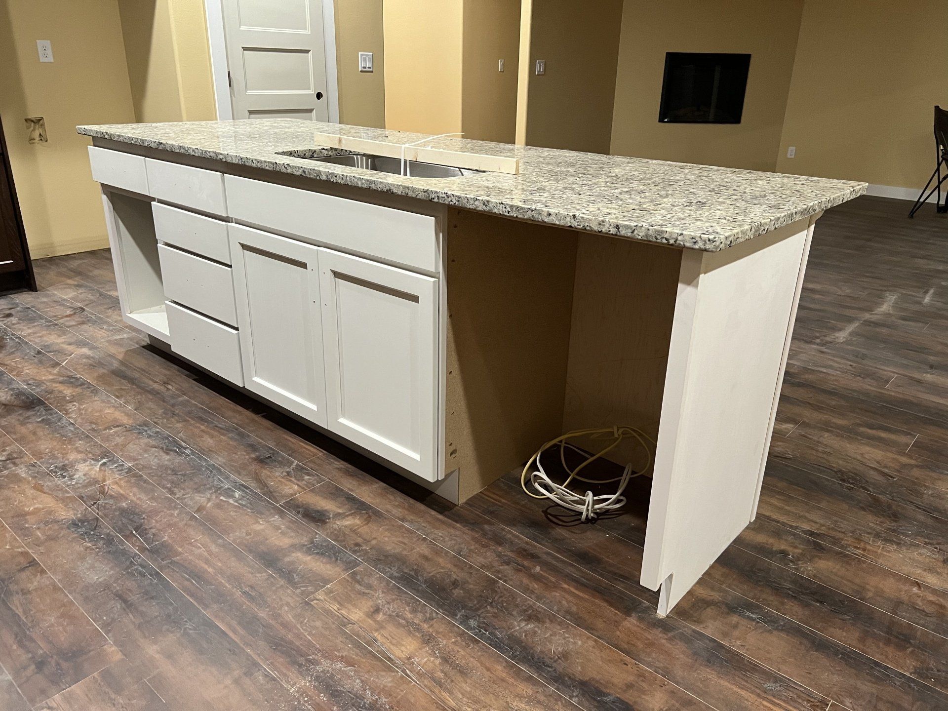 Kitchen island with white cabinets, granite countertop, and sink, in a room with hardwood floors.