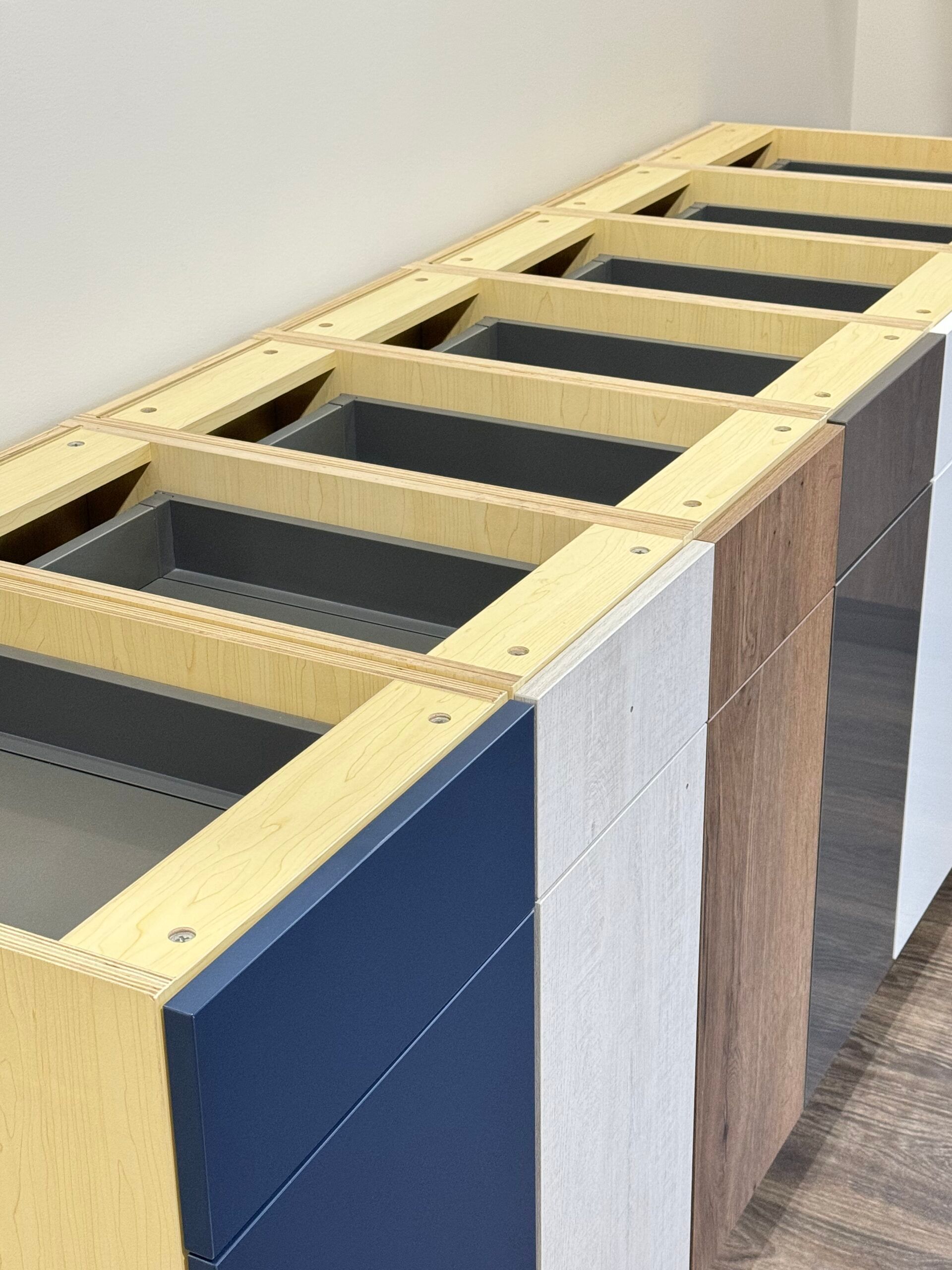 Wooden cabinet frames with painted front panels in blue, beige, brown, grey, and white.
