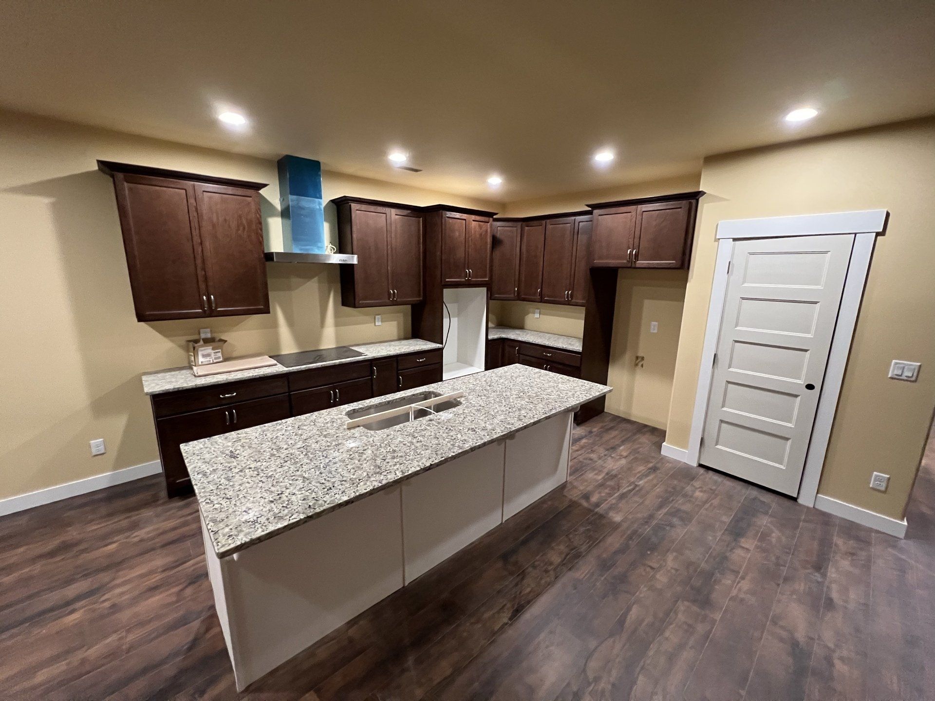Kitchen with dark brown cabinets, large island with speckled countertop, and hardwood floors.