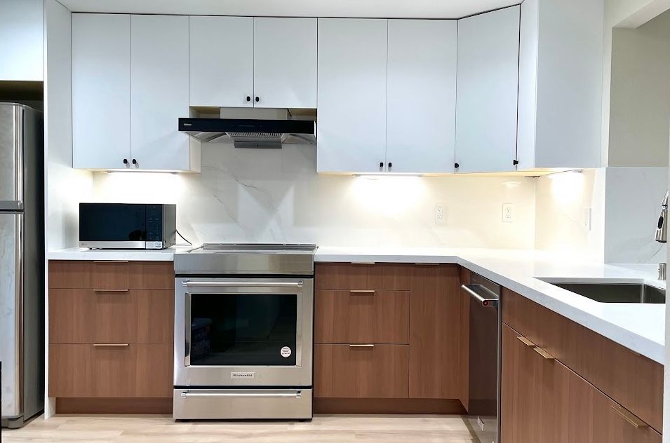 Modern kitchen with white and wood cabinets, stainless steel appliances, and under-cabinet lighting.