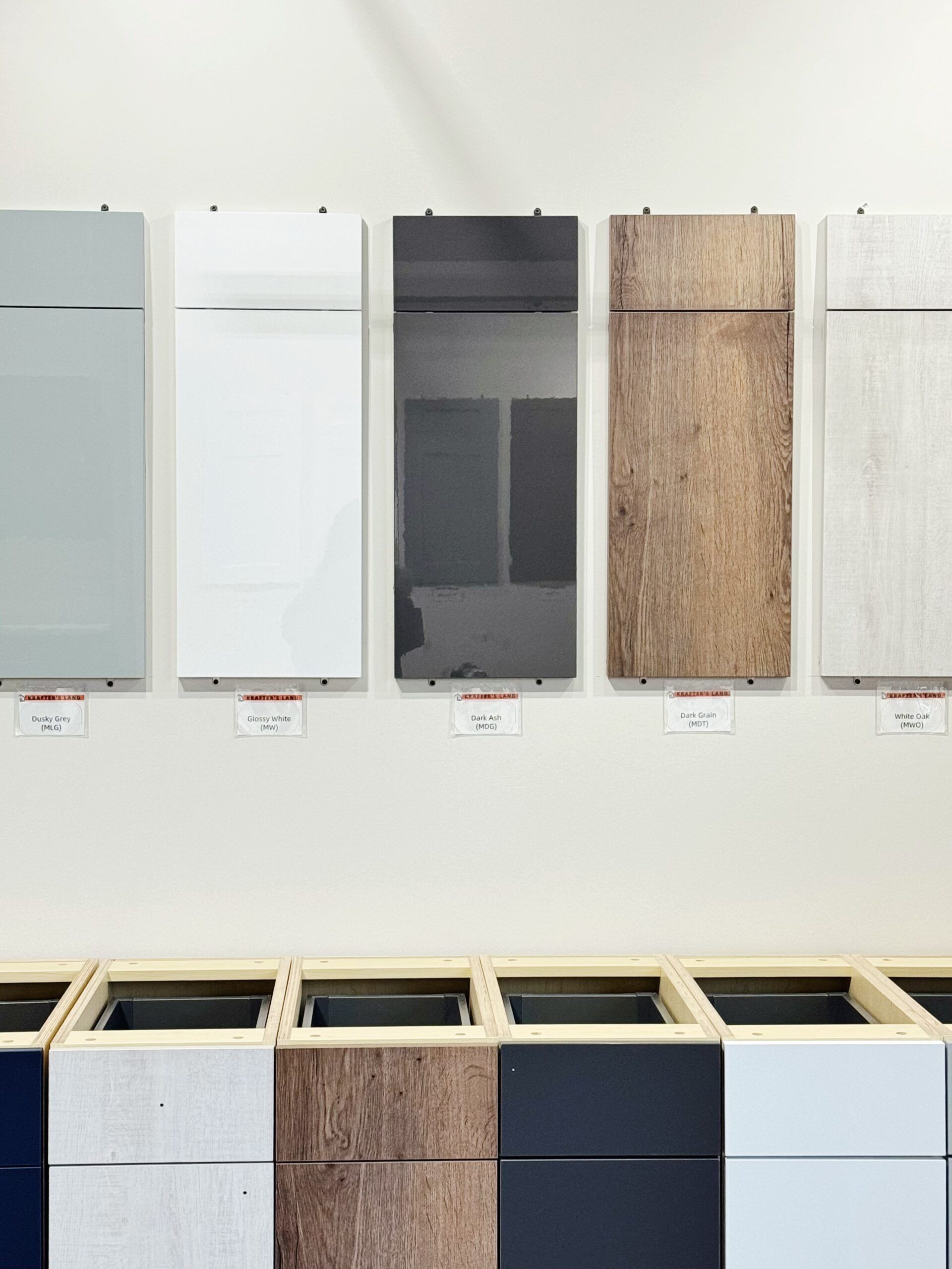 Cabinet door and drawer samples in various colors and textures displayed on a white wall.