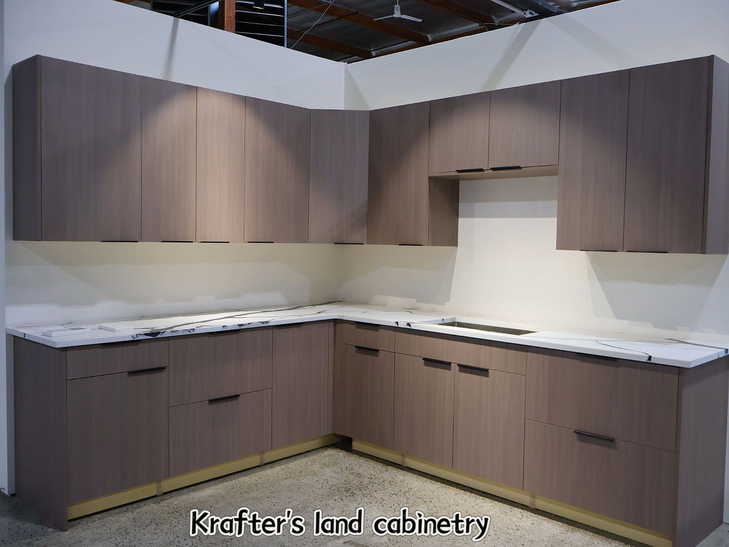 Modern kitchen with light brown cabinetry, marble countertops, and under-cabinet lighting.