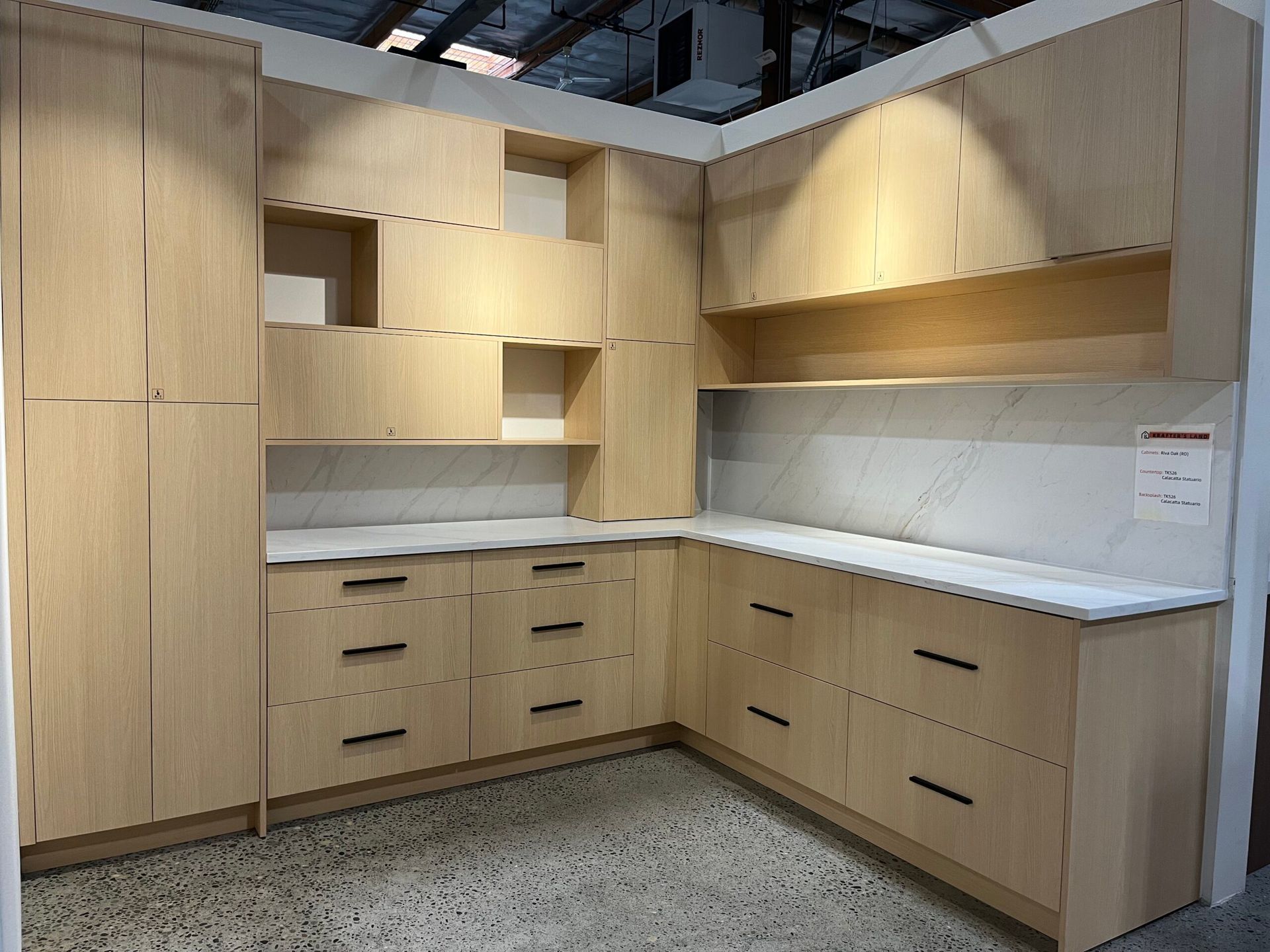 Light wood kitchen cabinets with black handles, white countertop, and backsplash.