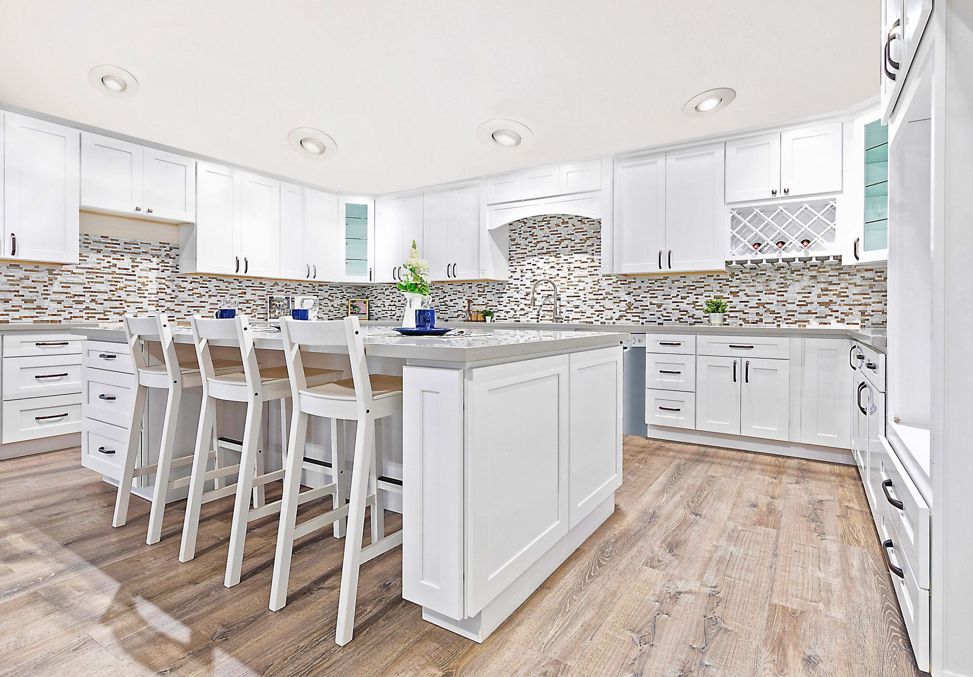 Bright white kitchen with island and bar stools, light wood floors, and neutral backsplash.