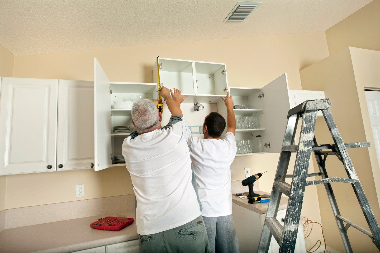 Two people installing a white kitchen cabinet, using a measuring tape.
