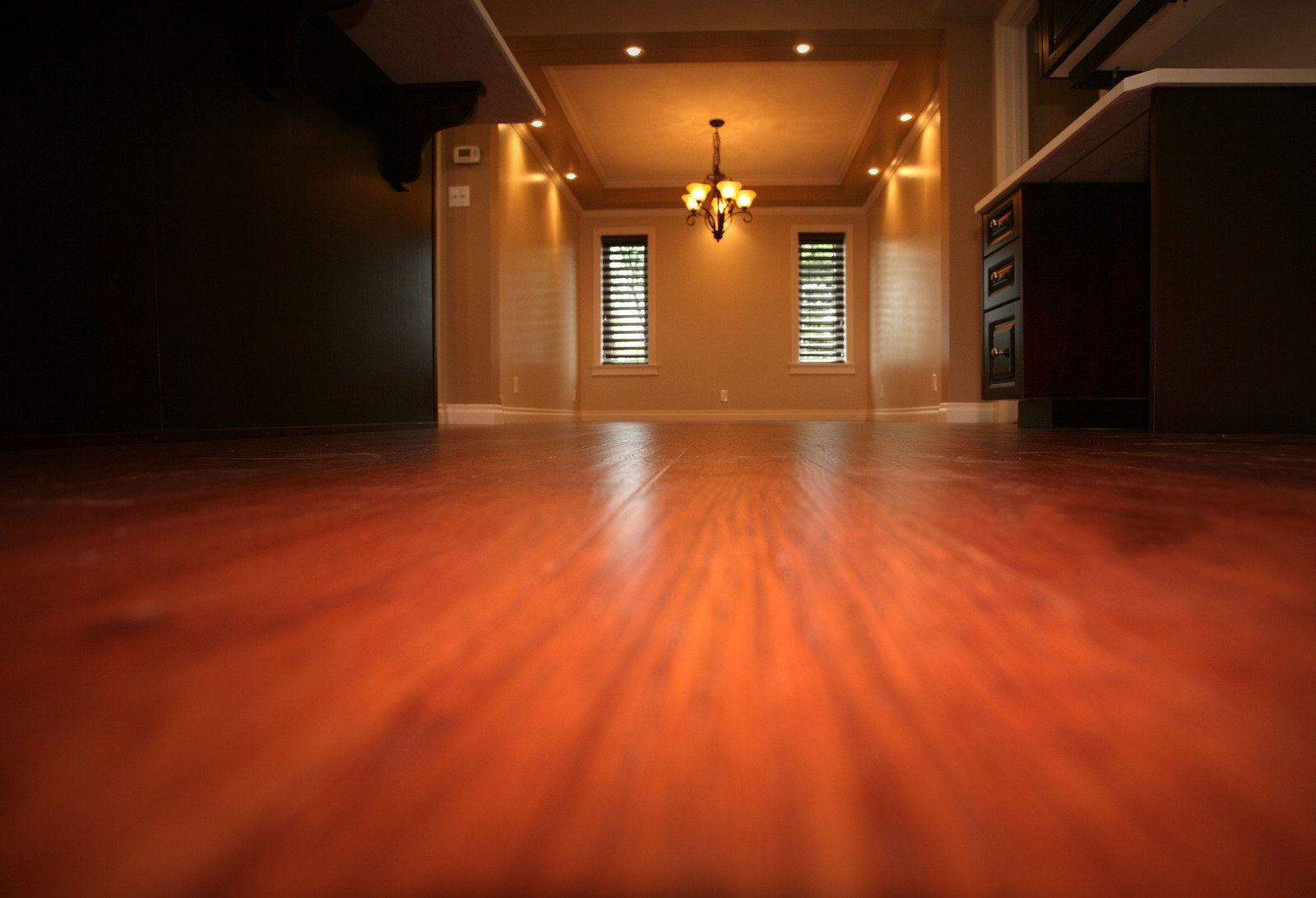 Wooden floor with light rays, leading to a room with windows and a chandelier.