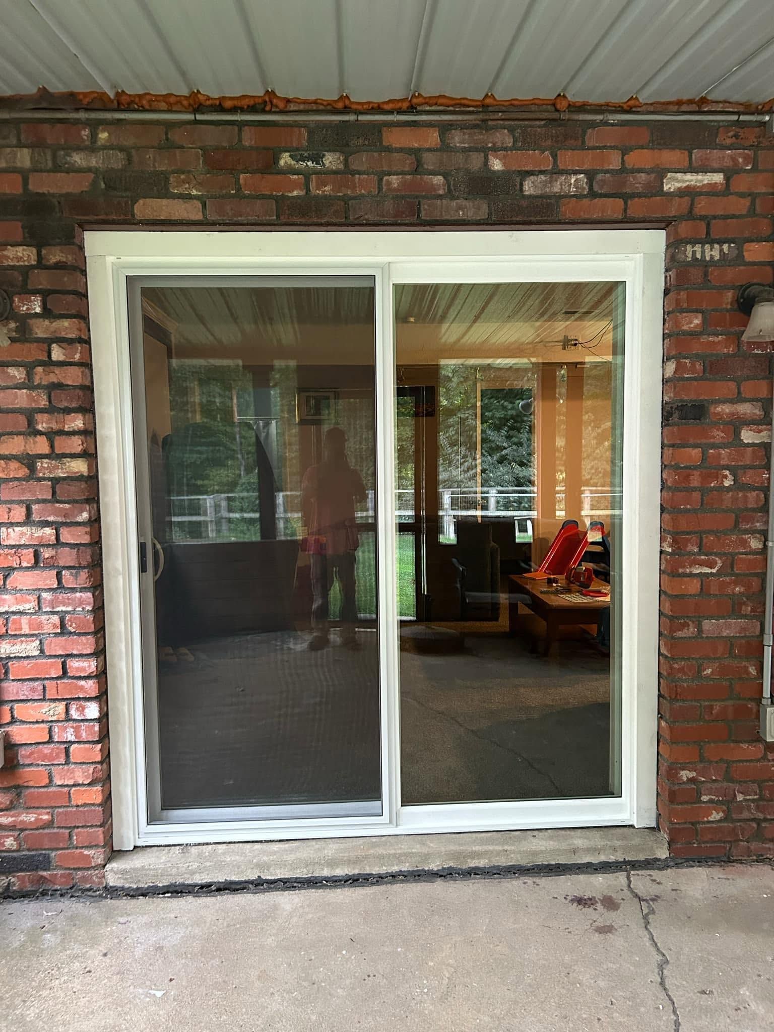 Sliding glass door in a brick wall, with a dark curtain and a view into a furnished room inside.