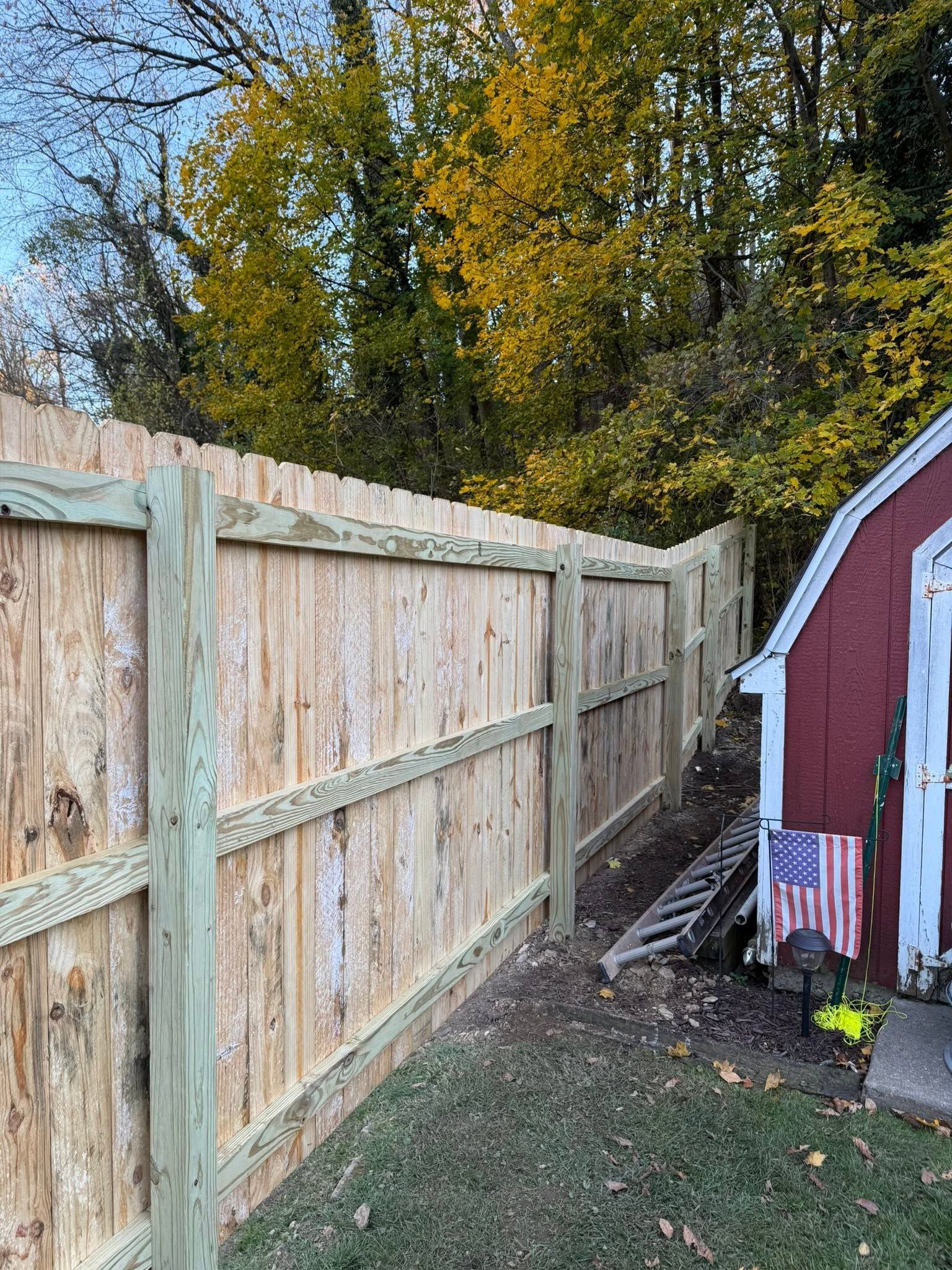 Weathered wooden fence beside a red shed in a backyard with trees and a small American flag on the ground