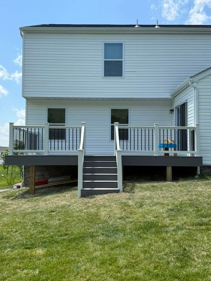 White two-story house with a raised deck, central stairs, and a grassy yard under a blue sky
