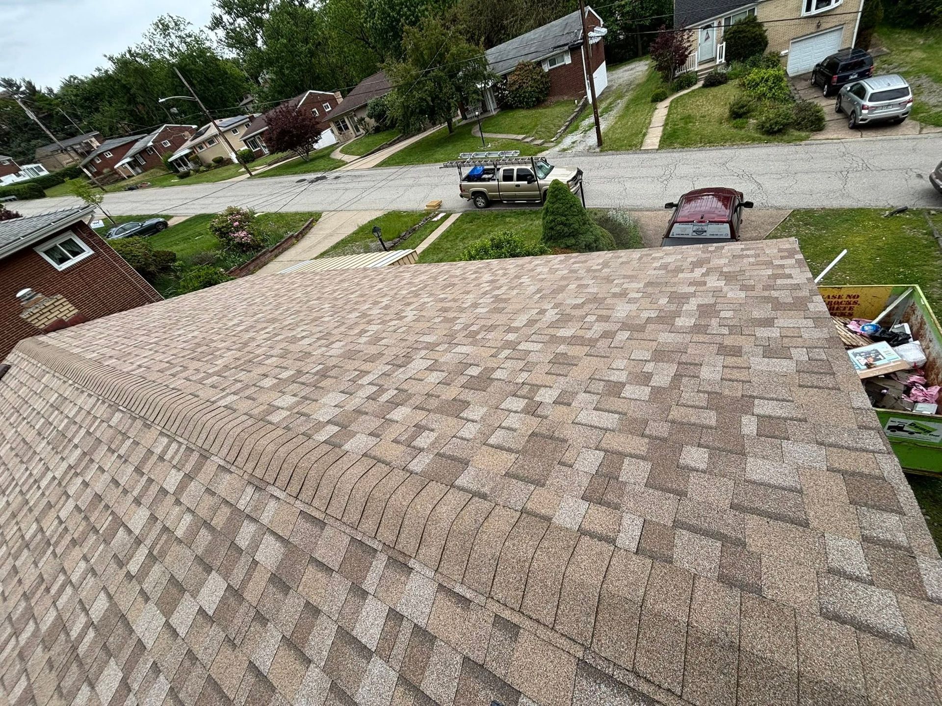 View from a roof over a suburban neighborhood street with parked cars and houses.