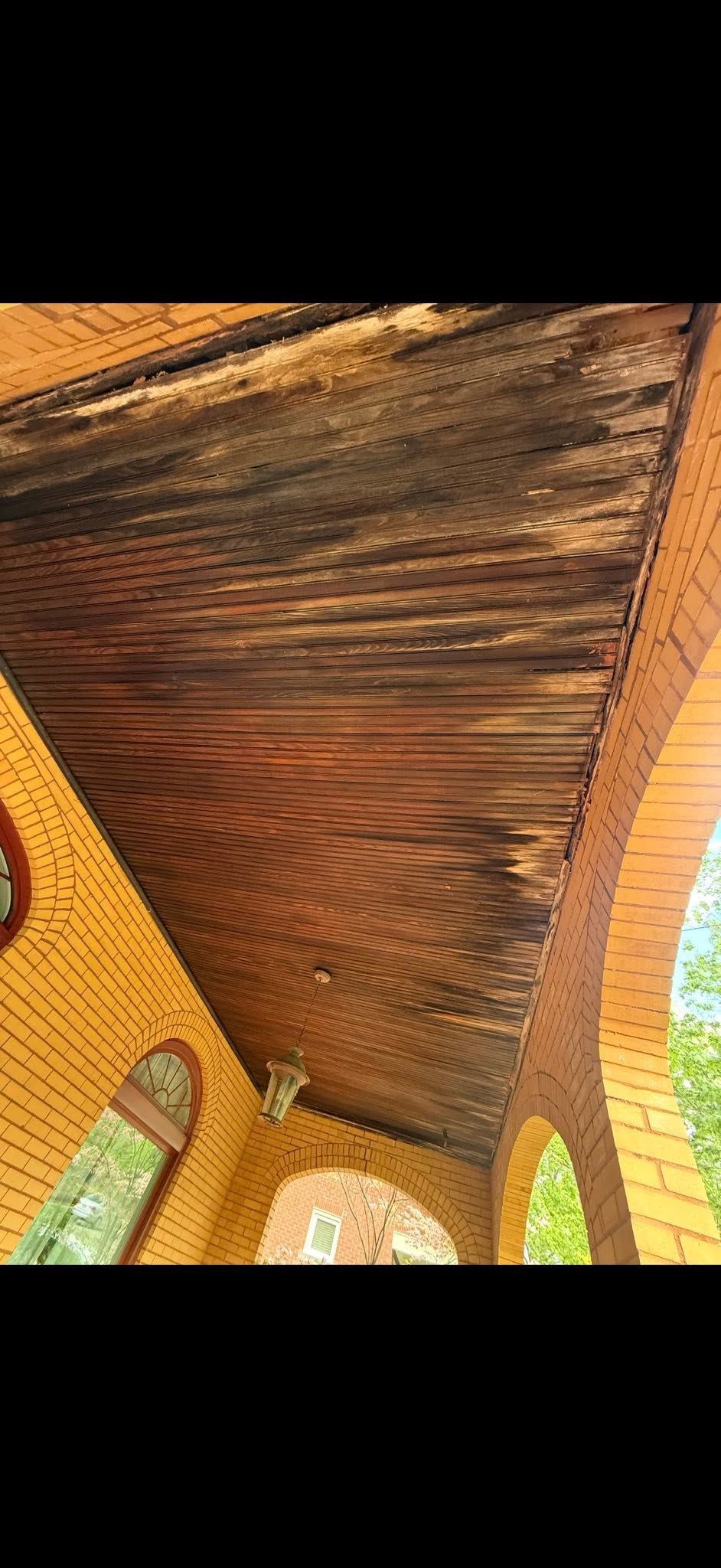 Wooden pavilion ceiling with woven texture and brick columns against a bright outdoor background