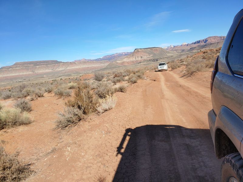 A car is driving down a dirt road in the desert