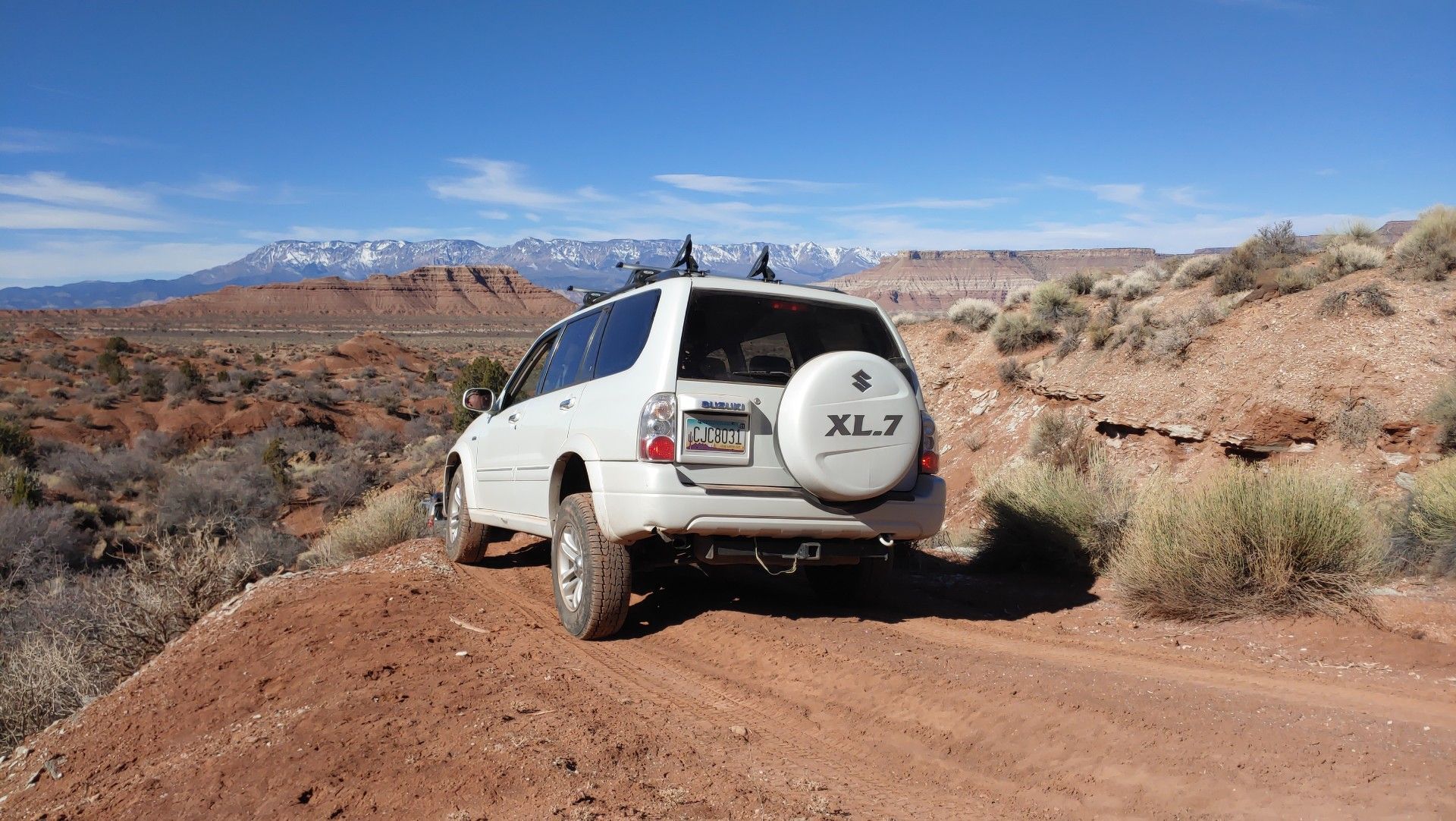 A white suv is parked on a dirt road with mountains in the background