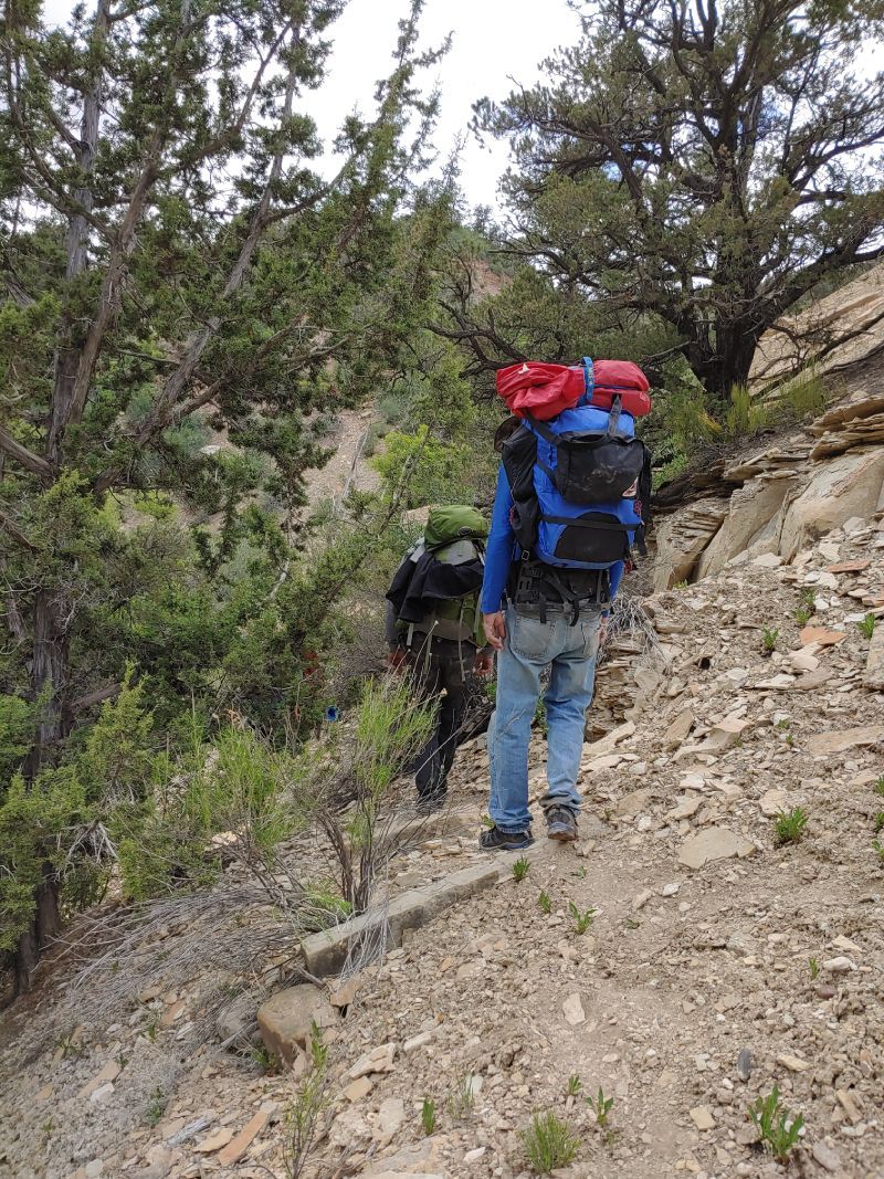 A man with a blue backpack is walking up a rocky hill