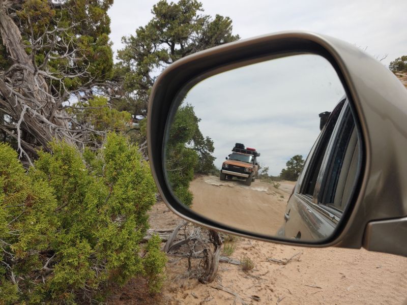 A car is driving down a dirt road in the rear view mirror