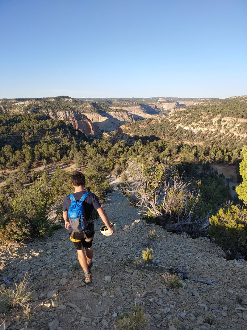 A man with a backpack is walking down a trail in the mountains