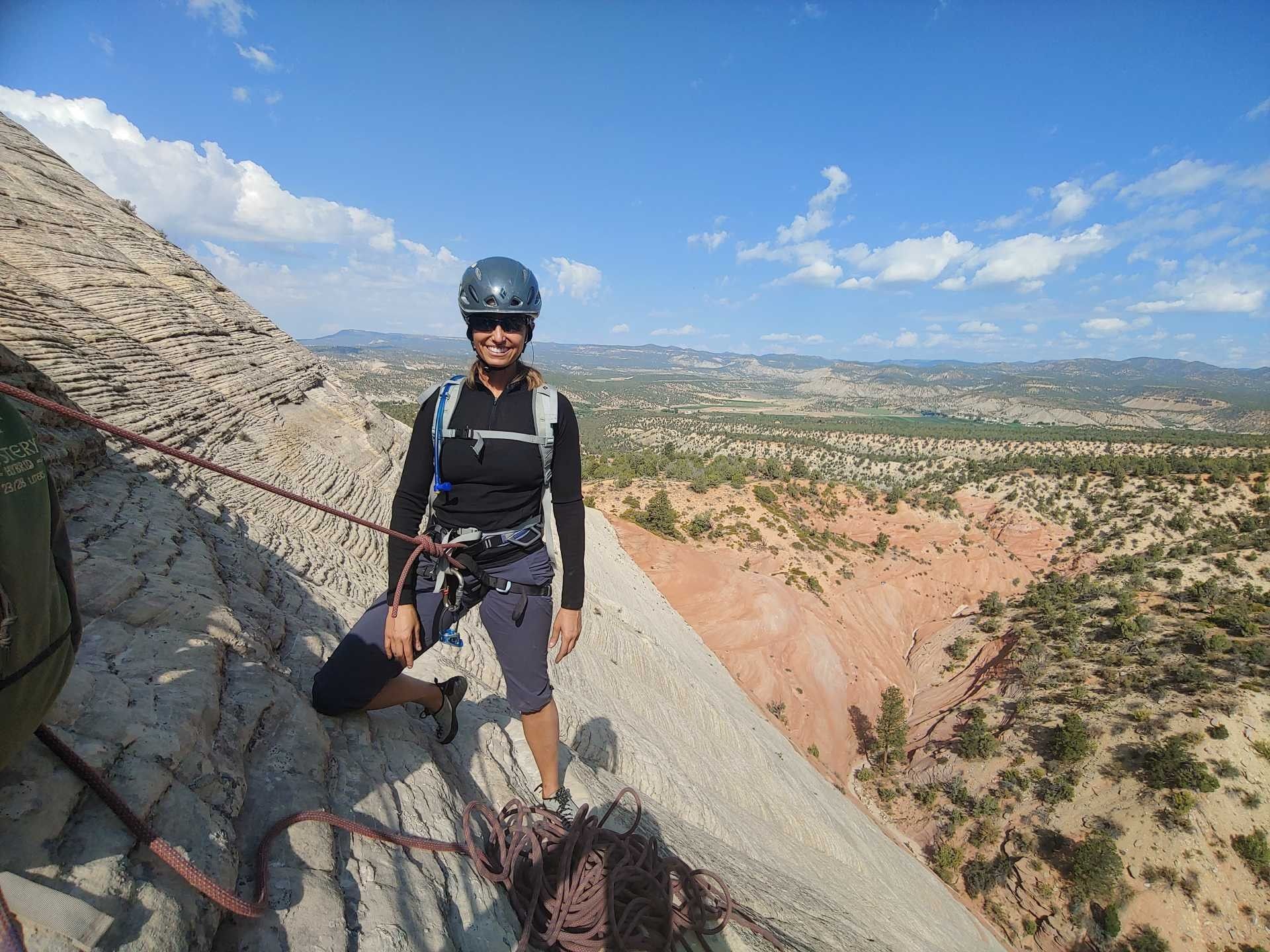 A woman wearing a helmet and sunglasses stands on top of a mountain