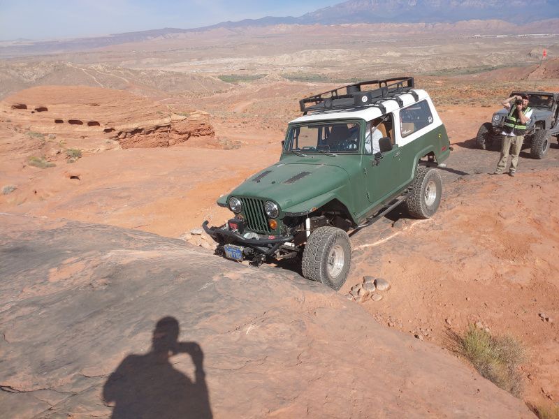 A green jeep is driving down a dirt road