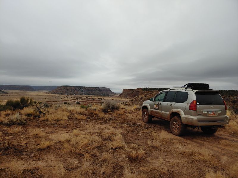 A silver suv is parked on the side of a dirt road in the desert.