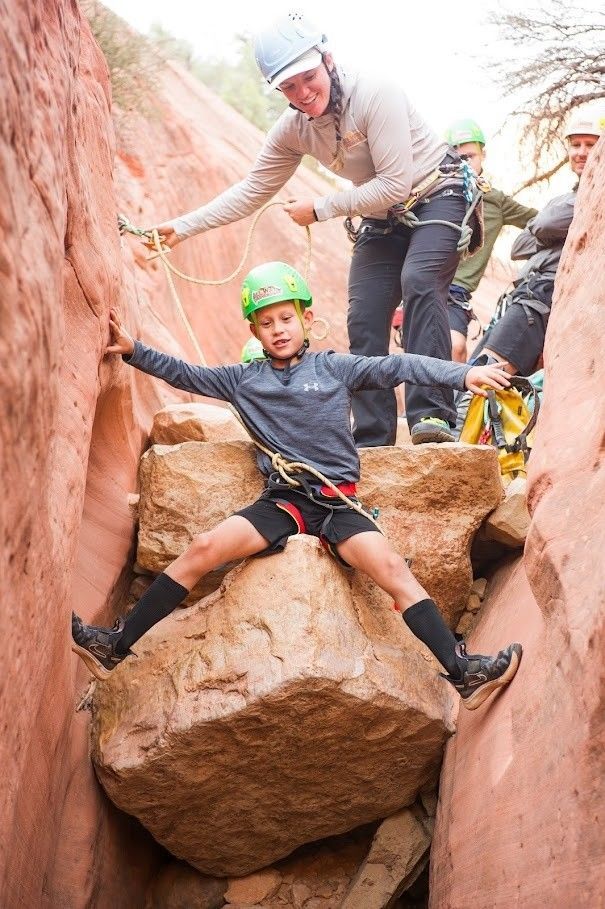 A woman is helping a young boy climb a rock.