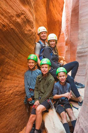 A family is sitting on a log in a canyon wearing helmets.