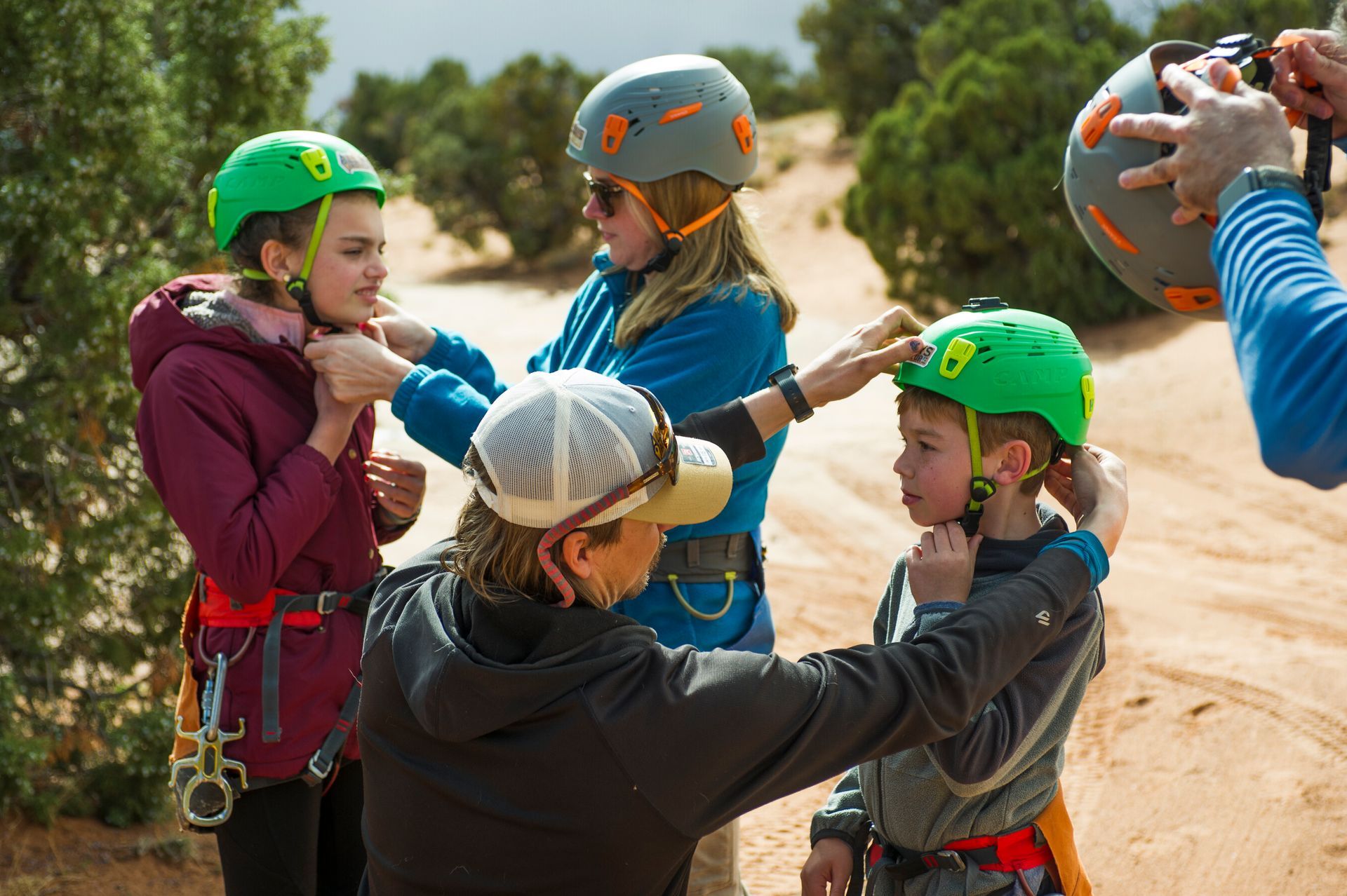 People adjusting helmets on children wearing harnesses, preparing to climb outdoors.