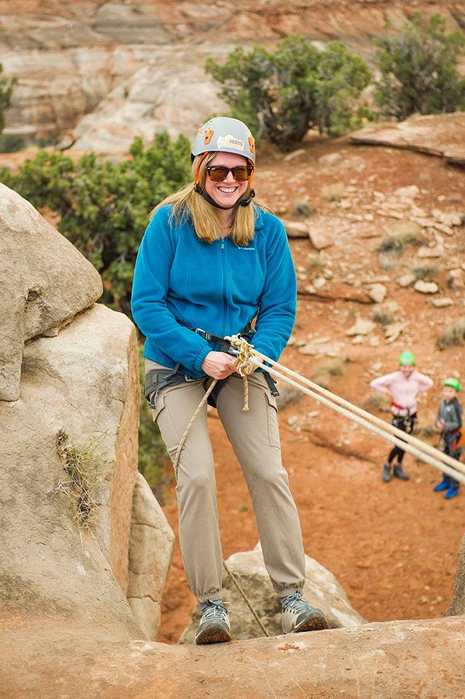 A woman wearing a helmet and sunglasses is holding a rope on a rock.