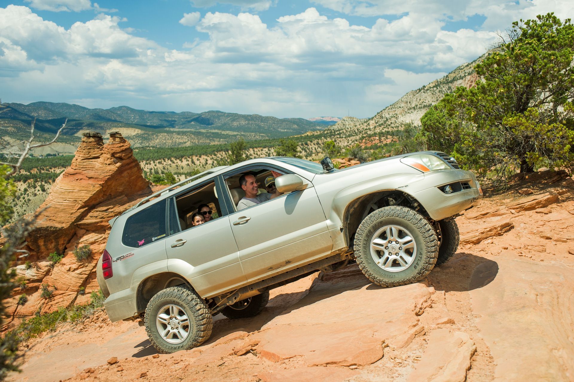 A silver suv is driving down a dirt road