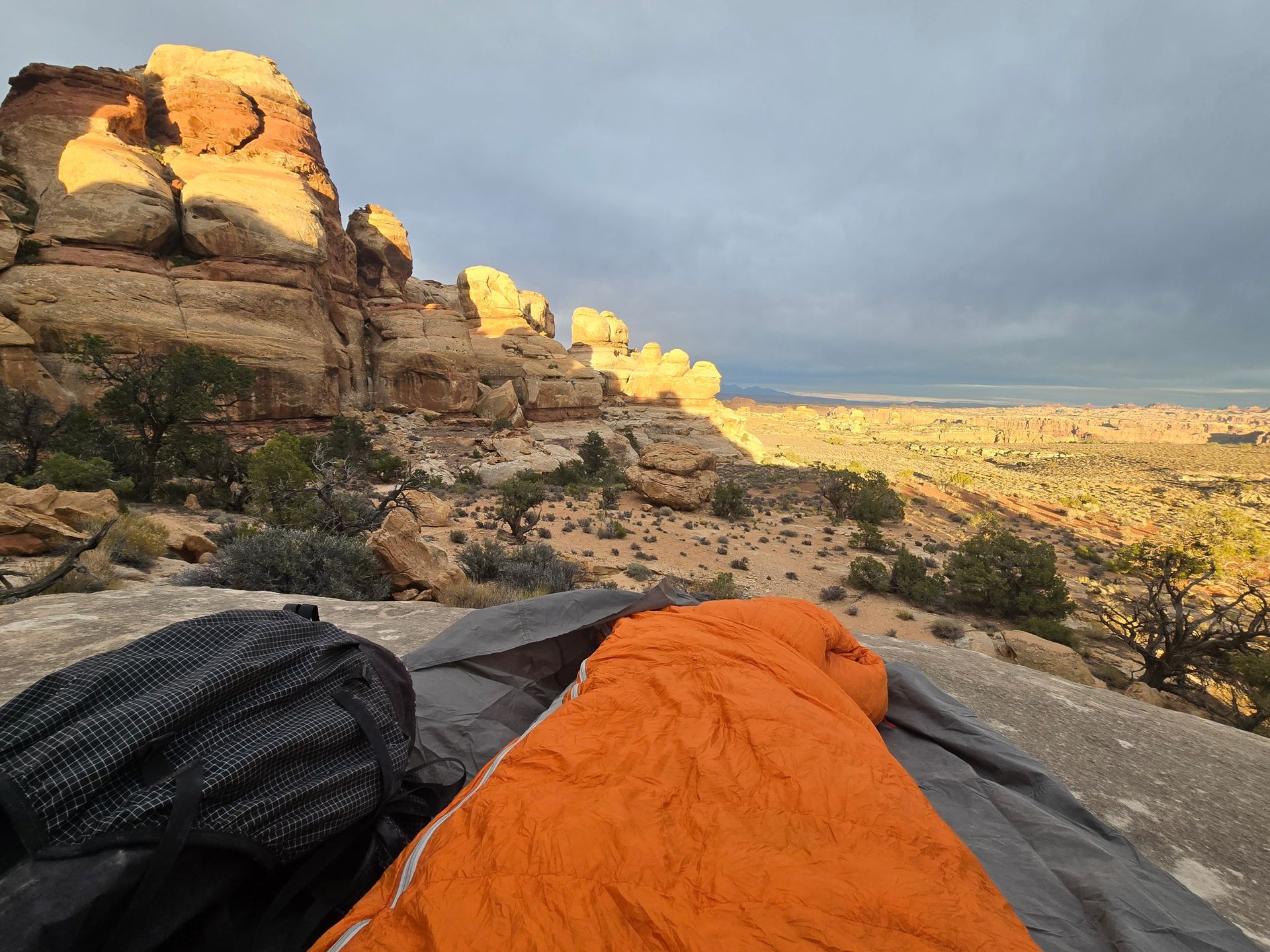 Orange sleeping bag on a rock with a scenic desert canyon view at sunrise.