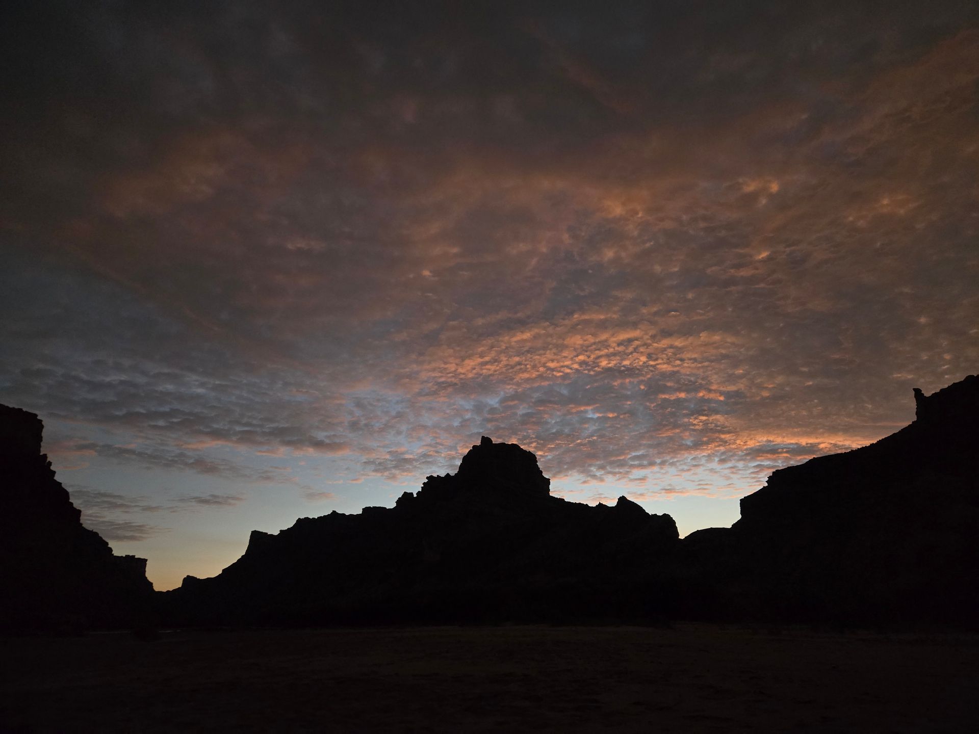 Silhouette of mountains against a colorful sunset sky with shades of orange and pink.