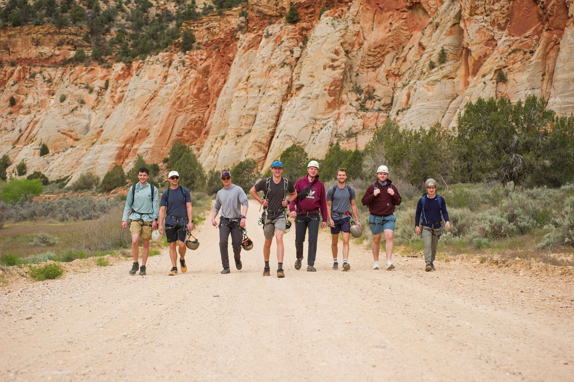 Hikers walking on a dusty trail beside layered red rock cliffs