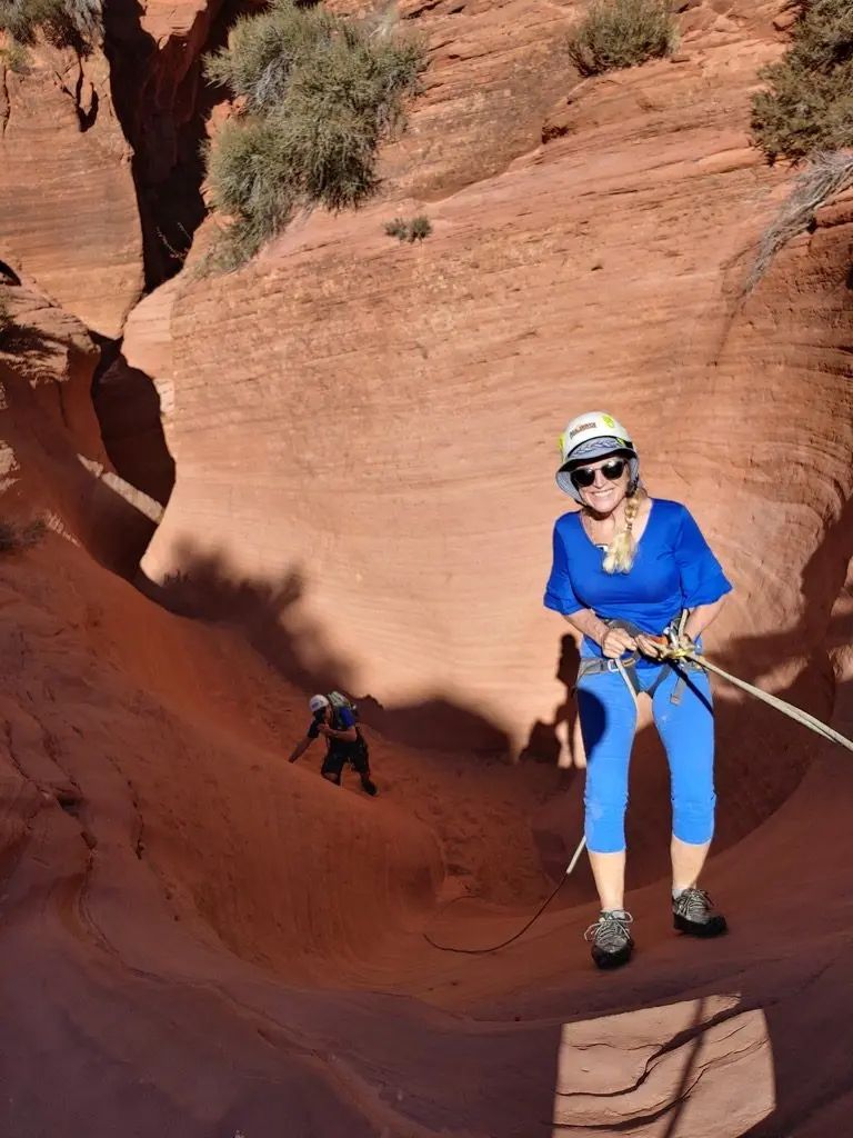 A woman in a blue shirt is holding a rope in a canyon