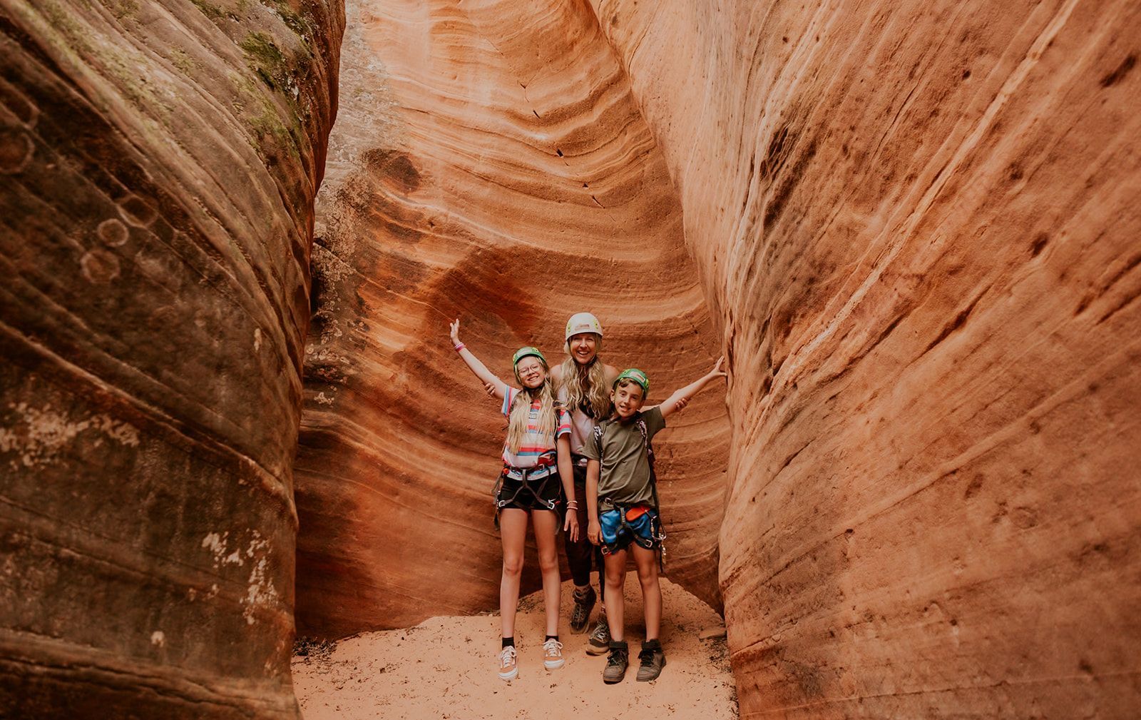 Three people stand inside a narrow, orange-walled sandstone canyon, smiling and posing for a photo.