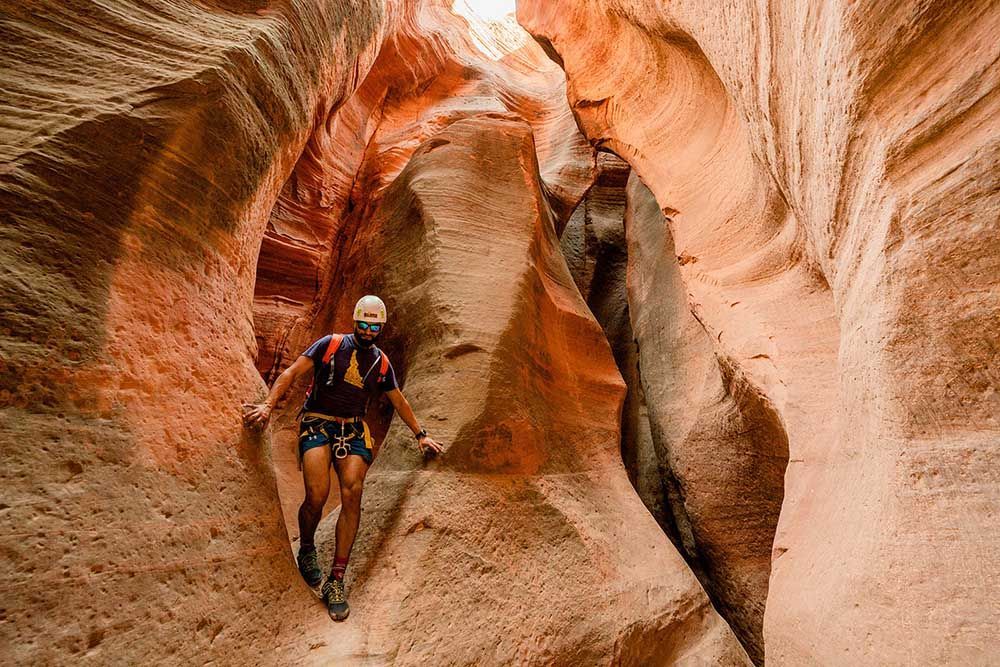 A man in a helmet is walking through a canyon.