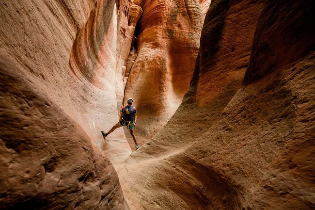A guest is posing in a stunning red rock slot canyon in Ladder Canyon near Zion National Park, guided by a professional from All Ways Adventure.