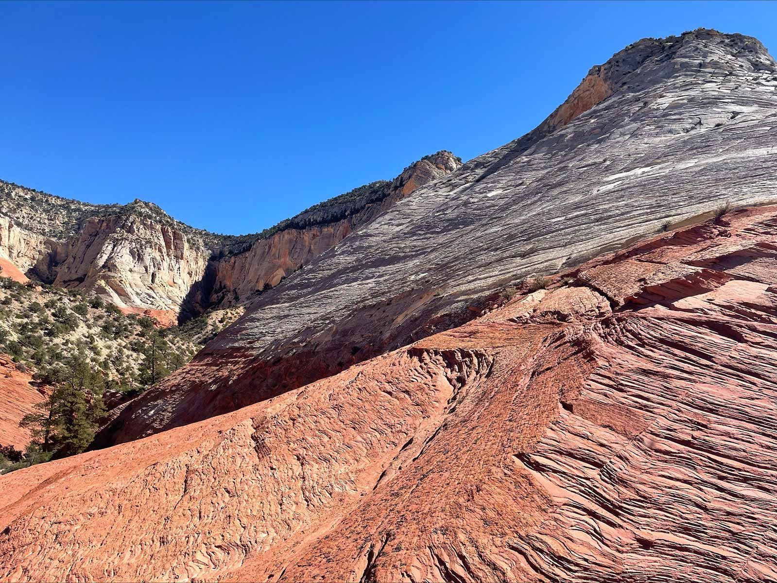 Red rock formations with layered white, black, and brown rock against a clear blue sky.