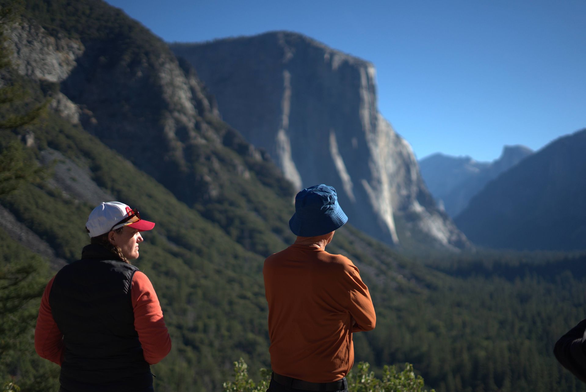 Two people overlooking a scenic valley with a large mountain in the background.