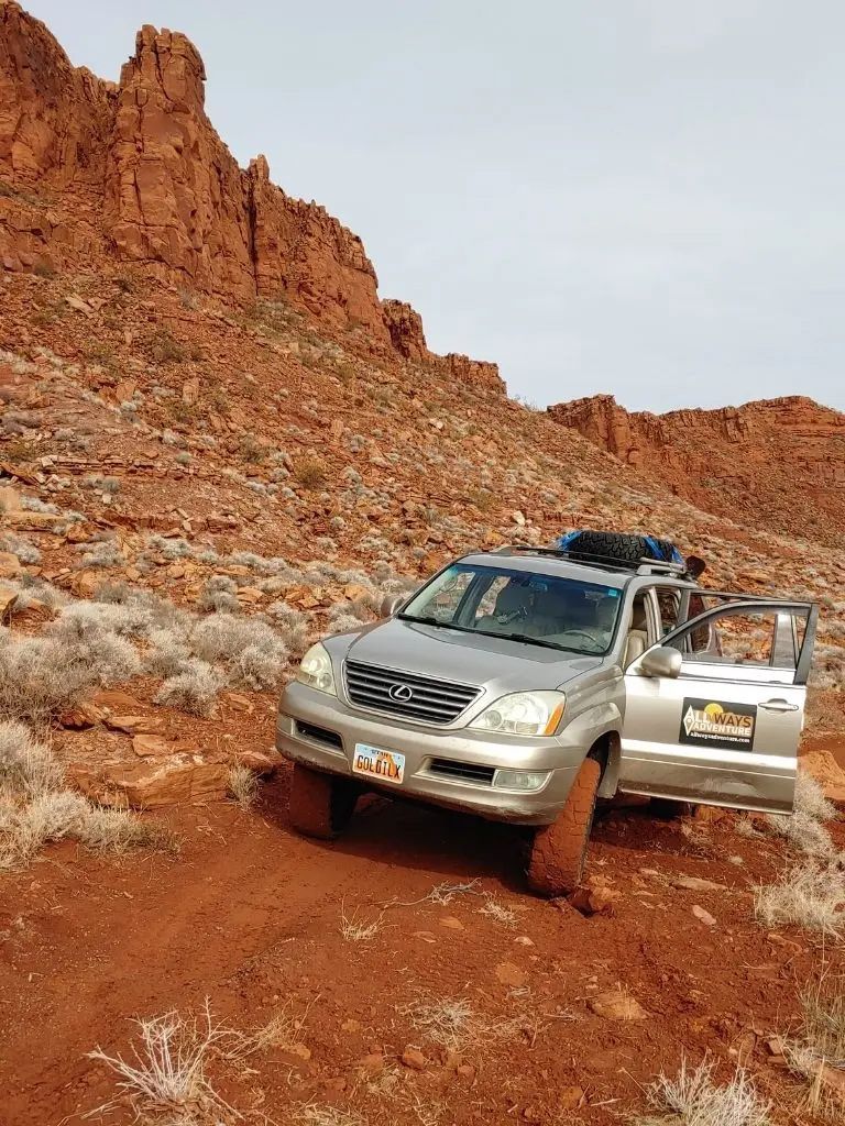 A silver suv is parked on a dirt road in the desert.