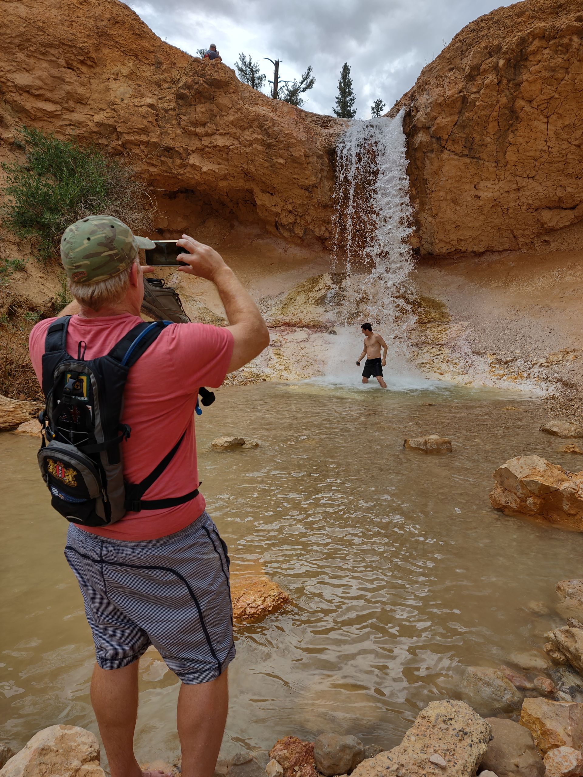 A man is taking a picture of a waterfall with his phone.