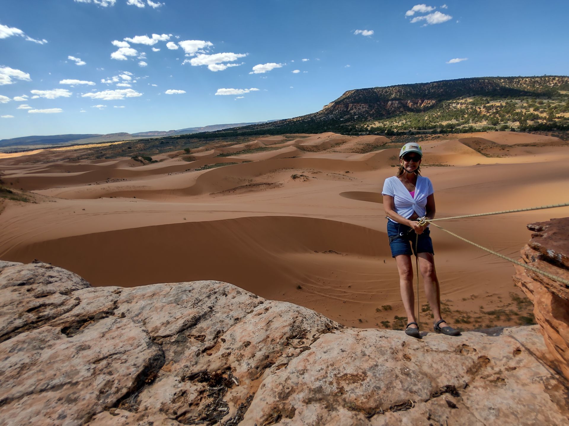 A woman is rappelling with Coral Pink Sand Dunes in the back ground.