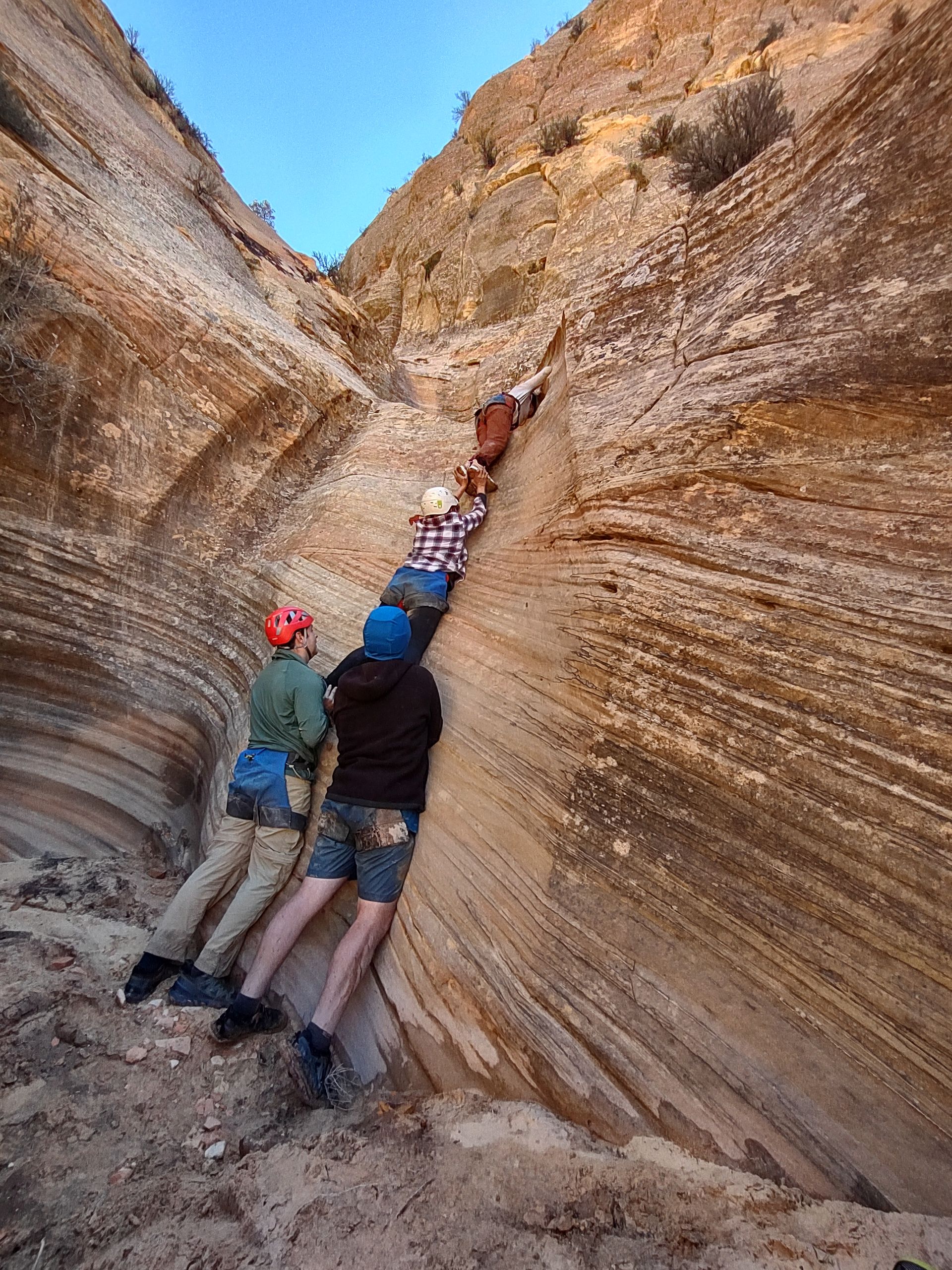 People climbing a narrow, striated sandstone canyon. They are roped together, moving upwards.