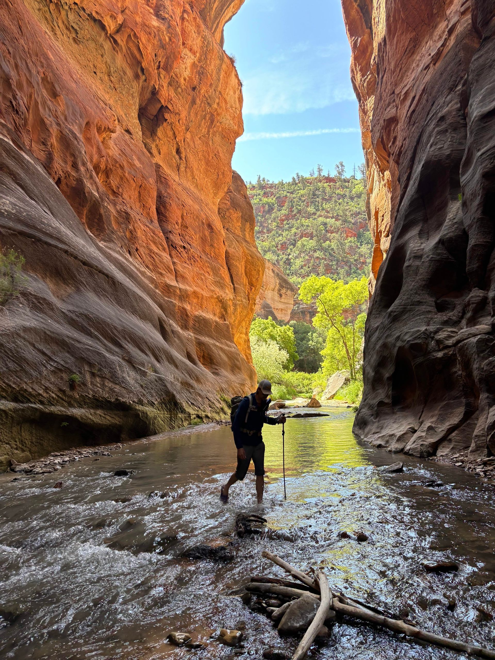 A person walks through a river flowing between red sandstone walls.