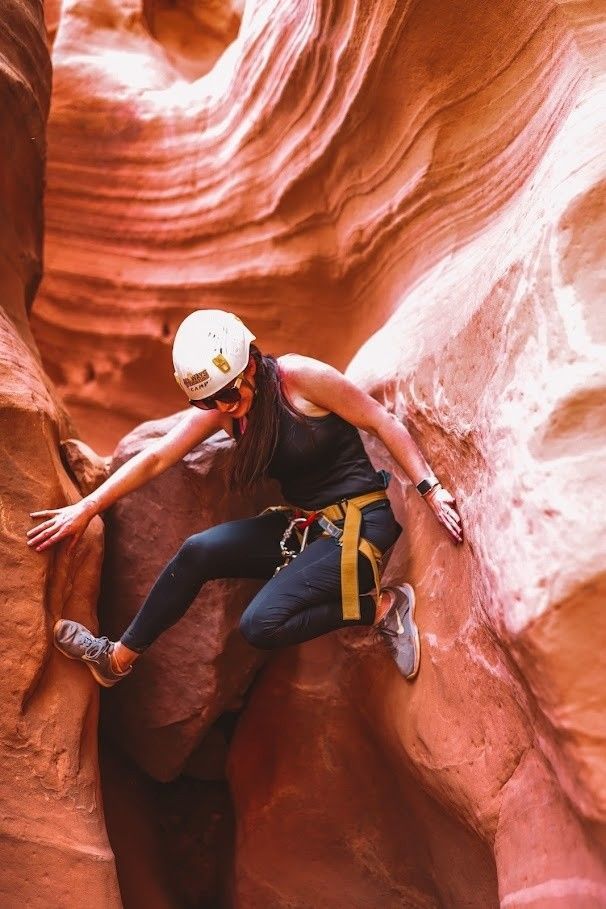 A woman is climbing up a rock wall in a canyon.