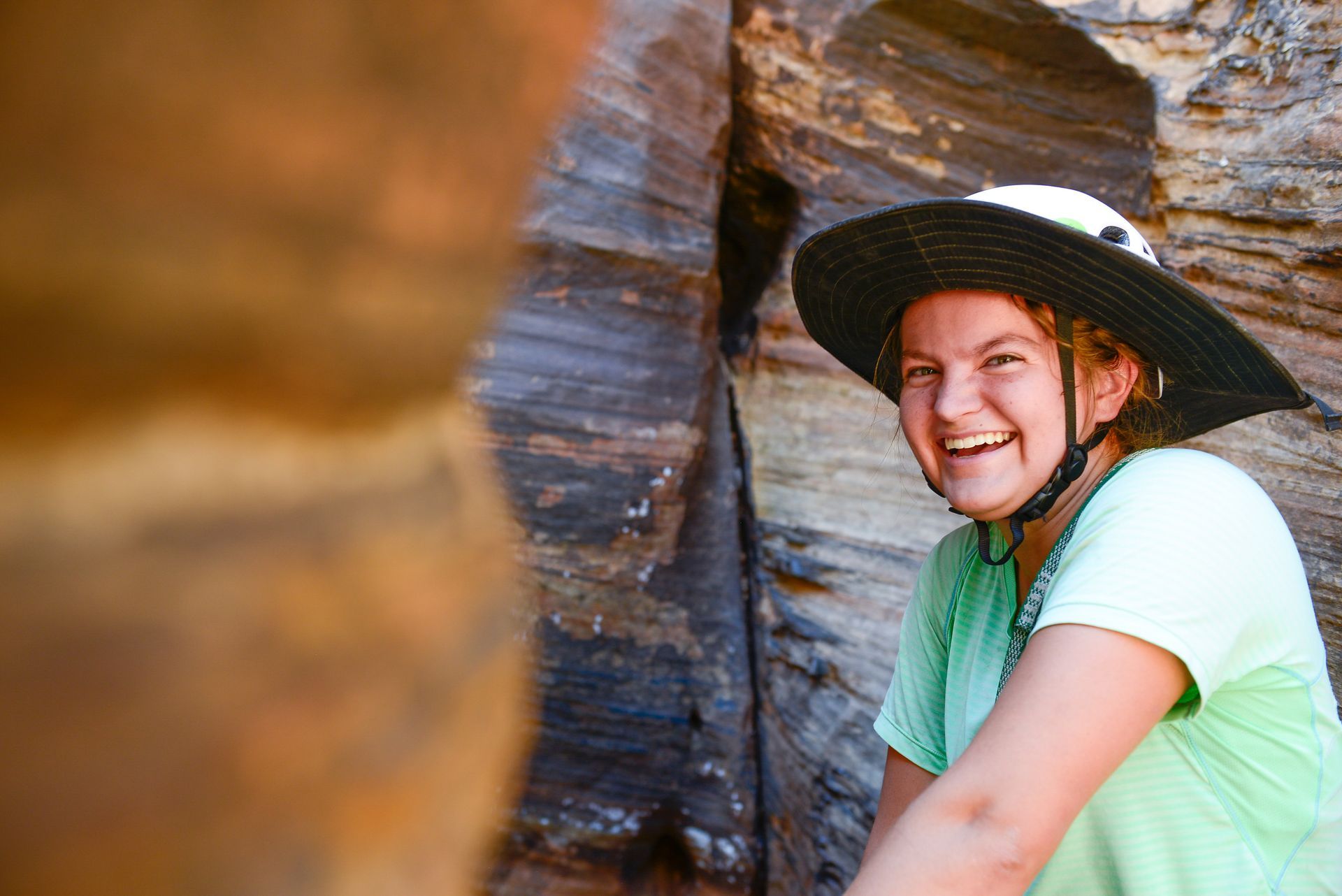 Woman in sun hat smiling by a rock wall.